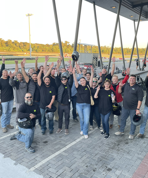 Group of McDonnel Group employees celebrating with raised hands, wearing matching black shirts and helmets, at a team-building event, highlighting company culture and camaraderie in construction careers.